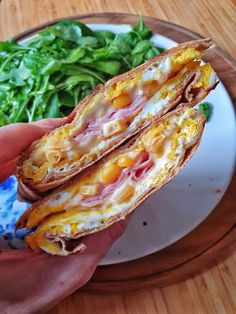 a person is holding a sandwich with cheese and ham on it next to a salad