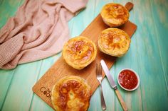 three mini quiches on a cutting board with ketchup and spoons next to them