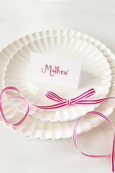 two white plates with pink ribbons and a name tag on them, sitting next to each other