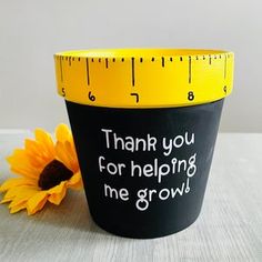 a yellow and black measuring cup with a sunflower next to it that says, thank you for helping me grow