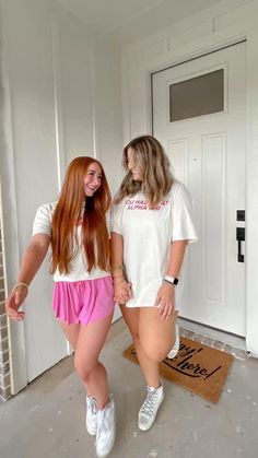 two women standing next to each other in front of a door wearing pink shorts and white t - shirts