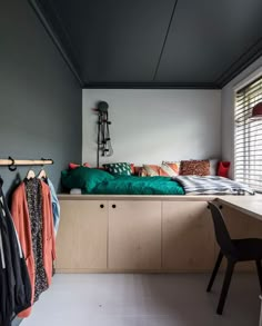 a bed sitting next to a window in a bedroom under a wooden shelf with clothes hanging on it