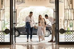 three adults and two children standing in front of an open door with a car behind them