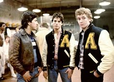 three young men standing next to each other in front of a group of people wearing jackets