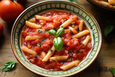 a bowl filled with pasta and sauce on top of a wooden table next to tomatoes