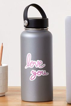 a gray water bottle with the words love you on it next to a white cup