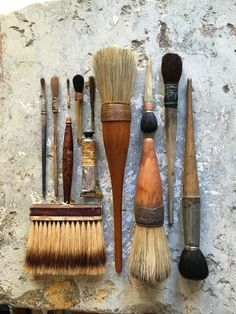 an assortment of different types of shaving brushes on a stone wall with paintbrushes