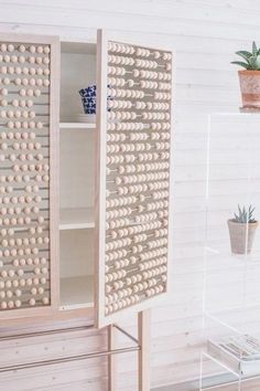 a wooden cabinet sitting next to a potted plant on top of a table in front of a white wall