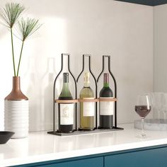 three bottles of wine and two glasses on a white counter top with blue cabinets in the background