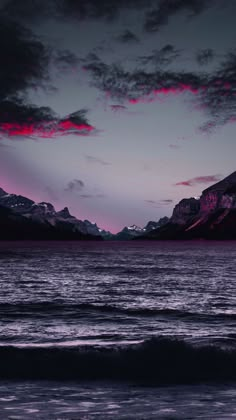 the sky is pink and purple as it sets over water with mountains in the background