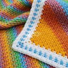 a multicolored crocheted blanket laying on top of a bed next to a pillow