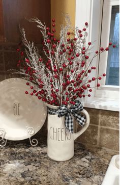 a white pitcher filled with red berries sitting on top of a counter next to a plate