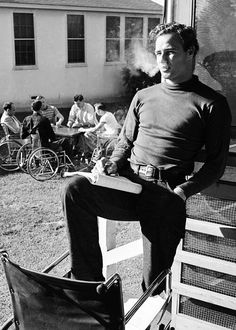 a man sitting on top of a wooden chair next to a building and people riding bikes