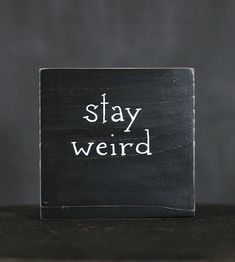 a black block with the words stay weird written on it