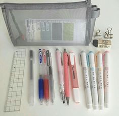 several pens and pencils sitting next to each other on a white table with a ruler