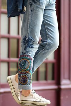 a woman's feet with colorful embroidered jeans and sneakers