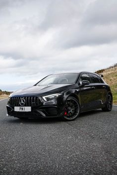 a black mercedes cla is parked on the side of the road with cloudy skies in the background