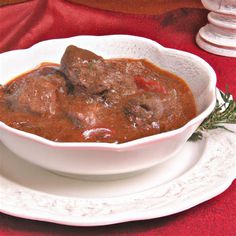 a white bowl filled with meat and gravy on top of a red table cloth