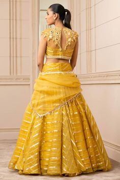 Mustard sheer brocade lehenga with a cascading drape and pearl detailing on the waistband. Paired with embroidered with resham, mirror work blouse. Comes with a matching sheer scarf embellished with fringes.
Component: 3
Pattern: Embroidered
Type Of Work: Mirror
Neckline: Round
Sleeve Type: Cap Sleeves
Fabric: Silk organza brocade stripes
Color: Yellow
Other Details: 
Embroidered blouse
Mirror and resham work
Tassel detail
Closure:
Blouse: Back concealed placket
Occasion: Destination Wedding - A Gold Fitted Organza Pre-draped Saree, Fitted Gold Organza Traditional Wear, Gold Fitted Organza Traditional Wear, Fitted Organza Lehenga With Intricate Embroidery, Organza Lehenga With Cutdana For Reception, Organza Choli With Cutdana For Reception, Gold Organza Choli With Unstitched Blouse, Reception Organza Choli With Cutdana, Gold Organza Choli With Cutdana