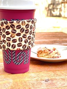 a pink coffee cup sitting on top of a wooden table next to a plate of food