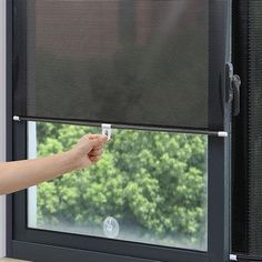 a person is opening the blinds in front of a window with their hand on it