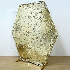 a large golden piece of art sitting on top of a hard wood floor next to a white wall