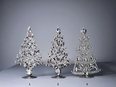 three crystal christmas trees are on display in front of a gray background with white dots