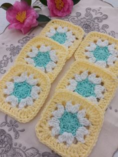 three crocheted squares sitting on top of a table with pink flowers in the background