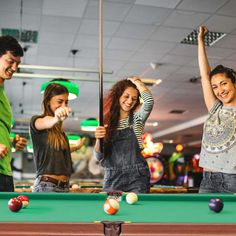 four young people playing pool in a billiards's room with one woman raising her arm up