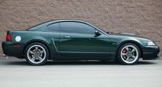 a dark green sports car parked in front of a tan brick wall with white rims