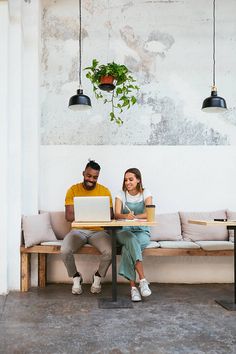 two people sitting at a table with laptops in front of them by the wall