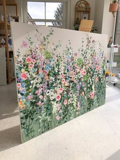 a painting is displayed on the floor in front of a window with flowers painted on it