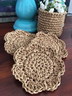 two crocheted flower pots sitting on a wooden table next to a blue vase