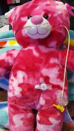 a pink and red teddy bear sitting on top of a pile of stuffed animals with tags attached to it's ears