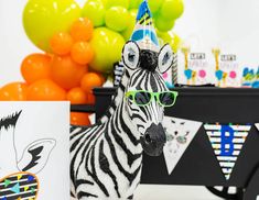 a zebra wearing glasses and a party hat with balloons in the background at a birthday party