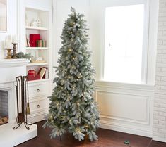 a white christmas tree in a living room next to a fire place and bookcase