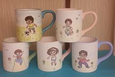 five coffee mugs with cartoon characters on them sitting on a blue tablecloth next to a wooden wall