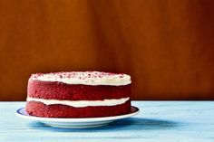 a red velvet cake with white frosting on a blue wooden table in front of a brown background