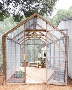 a small greenhouse with a metal roof and mesh walls on the inside, in front of a shed