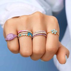 a woman's hand with five different colored rings on her fingers and one is wearing a white shirt