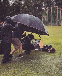 two people standing in the rain with an umbrella over their heads and one person laying on the ground