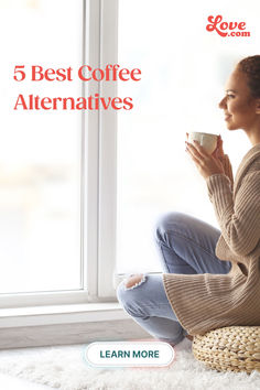 a woman sitting on the floor holding a coffee cup in her hand and looking out the window