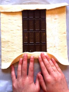 two hands reaching for the dough on top of a sheet of paper with chocolate bars in it