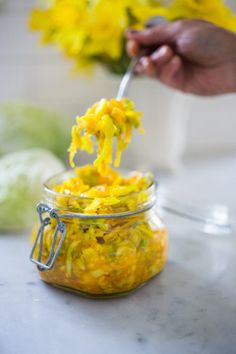 someone is spooning food out of a jar with yellow flowers in the back ground