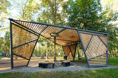 a wooden structure in the middle of a park with benches and tables underneath it, surrounded by trees