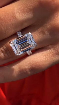 a woman's engagement ring with an emerald cut diamond in the center, on her finger