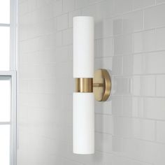 a white and gold bathroom light on the wall next to a window in a tiled room