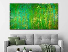 an abstract painting in green and yellow on a wall above a couch with two potted plants