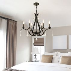 a chandelier hanging from the ceiling in a bedroom with white bedding and pillows