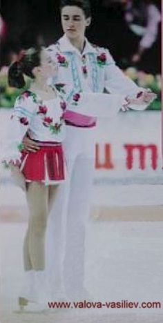 a man and woman standing next to each other in front of an olympic sign with flowers on it